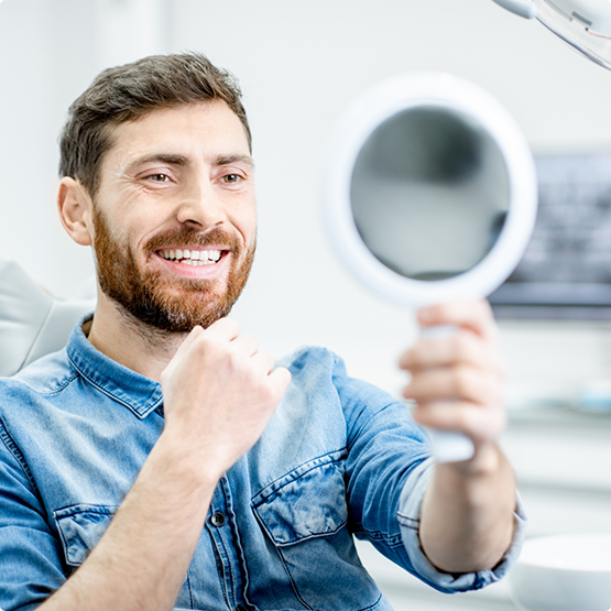 Bearded man checking smile in handheld mirror