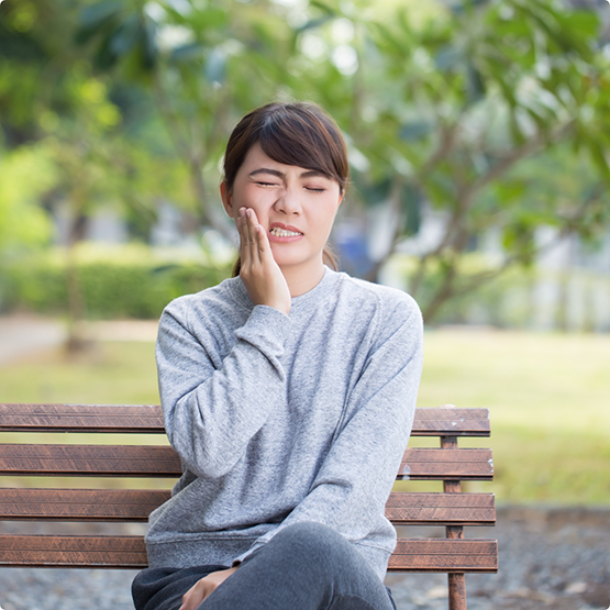 Woman with toothache sitting on bench rubbing jaw