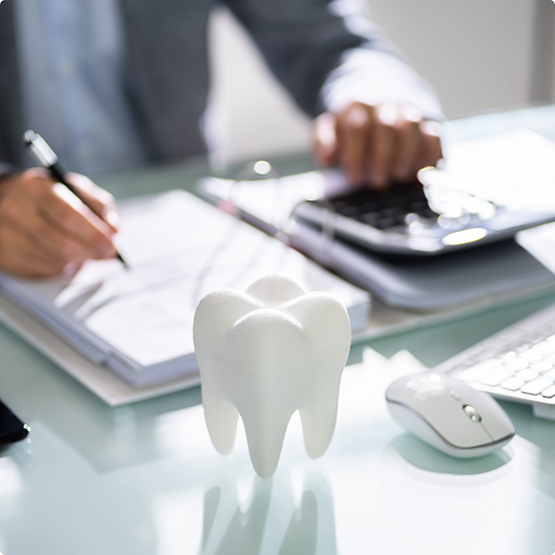 Fake tooth on table with patient using calculator and filling out forms in background