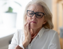 Woman with glasses rubbing jaw in pain