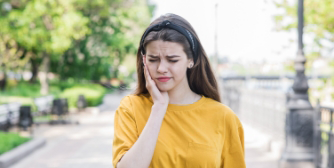 Girl in yellow shirt walking down street with tooth pain